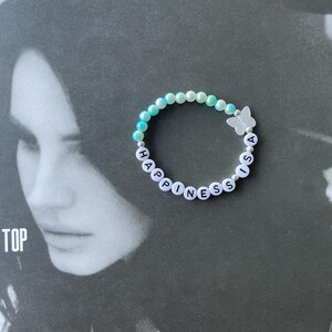 May include: A light blue and white beaded bracelet with the words "Happiness is a" spelled out in black letters. A silver butterfly charm is attached to the bracelet.