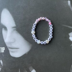 May include: A white beaded bracelet with the words "SAY YES TO HEAVEN" spelled out in black letters. The beads are pink, white, and iridescent.
