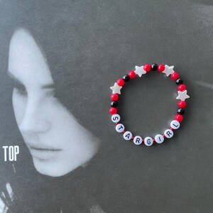 May include: A red and black beaded bracelet with white star-shaped beads spelling out "STARGIRL".