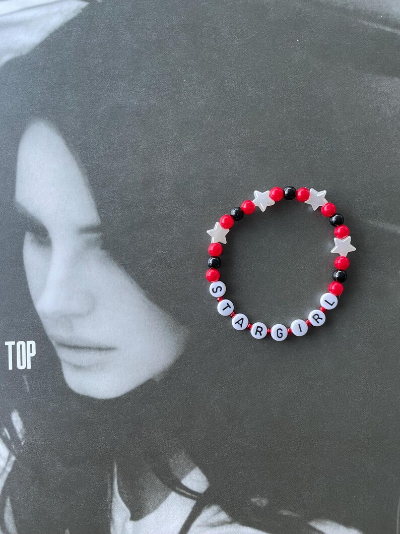 May include: A red and black beaded bracelet with white star-shaped beads spelling out "STARGIRL".
