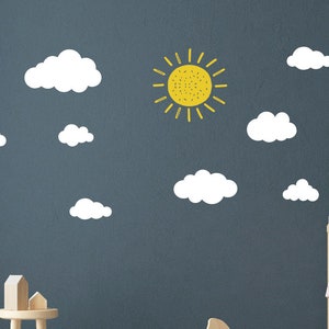 Puede incluir: Un sol amarillo con rayos y nubes blancas sobre un fondo azul oscuro. Este es un conjunto de calcomanías de pared para una guardería o habitación infantil.