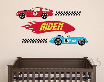 May include: A set of two race car wall decals with a checkered flag and the name Aiden in a red and yellow flame design. The cars are blue and red with racing numbers 7 and 8.