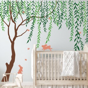 Könnte beinhalten: Ein Kinderzimmer mit einem braunen Baum und grünen Blättern an der Wand, einem weißen Babybett mit einer weißen Decke, einem Schaukelpferd und einem Korb mit einer schwarz-weiß gestreiften Decke.