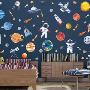 Può includere: Un muro blu con adesivi murali a tema spaziale. Gli adesivi includono pianeti, stelle, razzi, astronauti e un satellite. Il muro è decorato con un telescopio, uno scaffale in legno con libri e un pouf a righe.
