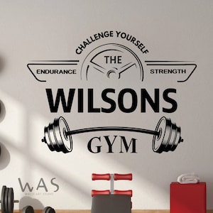 May include: Black and white gym wall decal with the text "Challenge Yourself" and "The" above a stylized weight with the text "Endurance" and "Strength" on either side. Below the weight is the text "Wilsons Gym".
