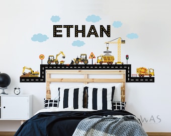 May include: A yellow construction vehicle wall decal set with a black road and the name "ETHAN" in black letters. The set includes a crane, a dump truck, a cement mixer, an excavator, and a bulldozer.