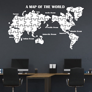 May include: A white puzzle piece world map wall decal with the names of continents and oceans. The decal is on a dark gray wall in an office setting.