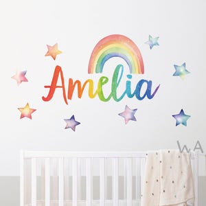 May include: A rainbow with a watercolour effect and the name Amelia written in a colourful script. The rainbow and name are surrounded by eight watercolour stars.