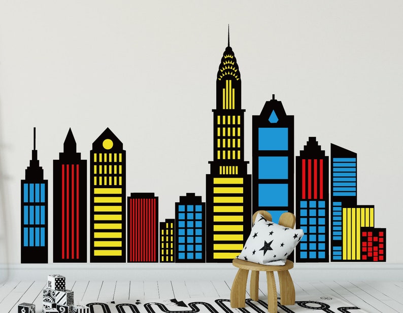 May include: Black and colorful silhouette of a city skyline with tall buildings. The buildings are in various shades of red, yellow, and blue. The skyline is on a white wall.
