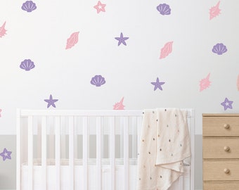May include: A white crib with a white blanket and a white wall with purple and pink seashells and starfish decals.
