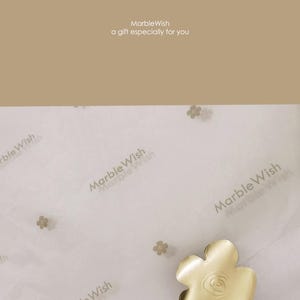 May include: A gold-colored, flower-shaped object with a rose design in the center, resting on white tissue paper printed with "MarbleWish". The text "MarbleWish a gift especially for you" is at the top of the image.