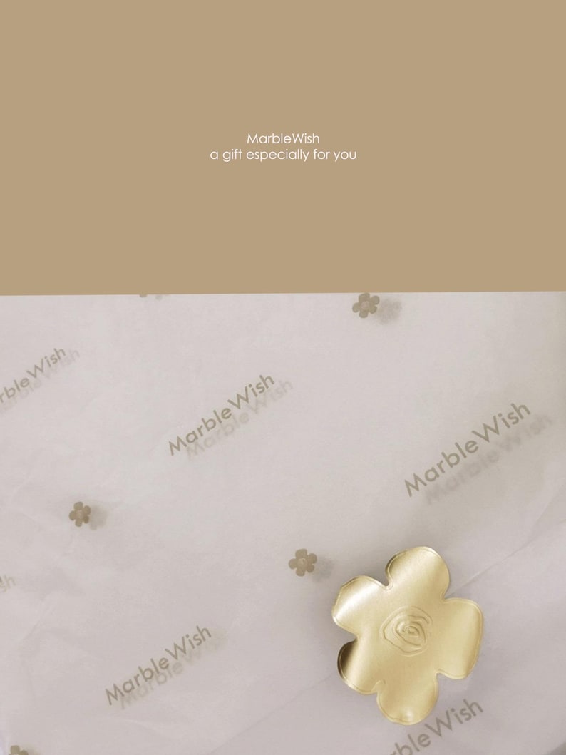 May include: A gold-colored, flower-shaped object with a rose design in the center, resting on white tissue paper printed with "MarbleWish". The text "MarbleWish a gift especially for you" is at the top of the image.