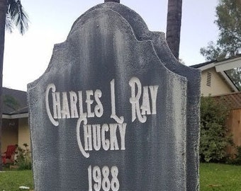 May include: A grey tombstone with the inscription "Charles L Ray Chucky 1988".