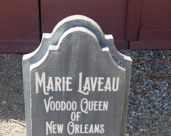 May include: A grey tombstone with the inscription "Marie Laveau Voodoo Queen of New Orleans".
