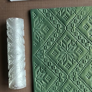 May include: A set of three polymer clay tools for creating embossed designs. The set includes a rolling pin with a geometric pattern, a sheet of green polymer clay with an embossed geometric pattern, and a wooden tool with a pointed tip.