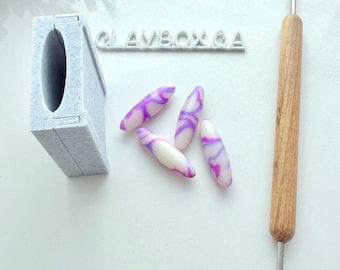 May include: A collection of polymer clay nail art supplies. The image shows four white and purple swirled nail art pieces, a gray nail art tool, a wooden handled tool, and a gray nail art holder. The text "CLAYBOX 6A" is also visible.