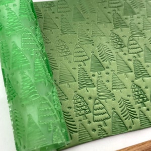 May include: A green rolling pin with a Christmas tree pattern is shown next to a sheet of green fondant with an embossed Christmas tree pattern.