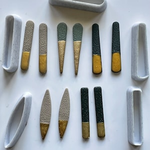 Op de afbeelding: Een set van 10 handgemaakte keramische oorbellen in verschillende vormen en kleuren. De oorbellen zijn geschilderd met gouden accenten en hebben een gespikkelde textuur. De oorbellen worden gepresenteerd op een wit oppervlak.