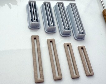May include: Set of seven white and brown plastic rectangle-shaped cookie cutters. The cutters are arranged in two rows. The top row has three cutters with a single line in the middle. The bottom row has four cutters with two lines in the middle.