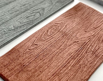 May include: Two wood grain textured silicone mats, one gray and one brown. The mats are designed to be used for creating realistic wood grain effects on fondant or other edible materials.