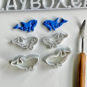 Op de afbeelding: Een set van zes koekjesvormen in de vorm van orka's. De vormen zijn wit en gemaakt van plastic. Twee blauwe orka koekjesvormen zijn ook inbegrepen.