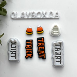 Peut inclure: Un ensemble de six emporte-pièces en plastique blanc avec les mots "Trick" et "Treat" en noir et orange. L'ensemble comprend également deux emporte-pièces en forme de maïs sucré.