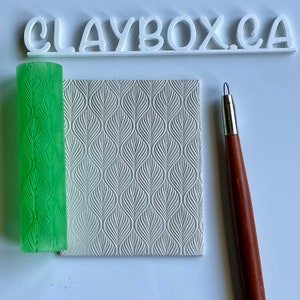 May include: A white silicone rolling pin with a green leaf pattern, a white silicone sheet with a leaf pattern, and a wooden tool with a metal tip. The text "CLAYBOX.CA" is visible in the background.