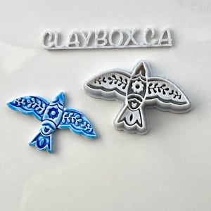 Peut inclure: Deux emportes-pièces en céramique en forme d'oiseau, l'un bleu et blanc et l'autre blanc. L'emporte-pièce blanc est un moule pour l'emporte-pièce bleu et blanc. Les emportes-pièces sont sur une surface blanche avec le texte "CLAYBOXCA" au-dessus.