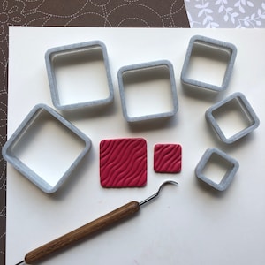 May include: A set of six square-shaped cookie cutters, a red and white patterned clay tile, and a small tool for crafting.