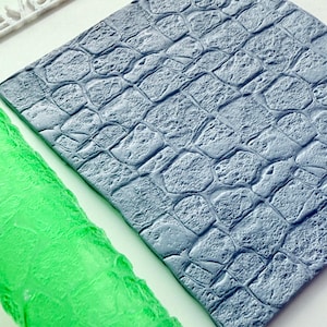 May include: Close-up of a textured, gray rectangular sheet with a repeating pattern resembling cobblestones. A green, textured roller is visible on the left. The image is well-lit, highlighting the details of the textures.