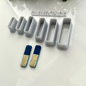 May include: Set of six rectangular polymer clay cutters in various sizes, with the text "CLAYBOX CA" on the top. Two small rectangular polymer clay earrings with a blue and gold design are also shown.