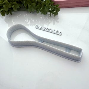 May include: White plastic cookie cutter shaped like a spoon. The cutter has a textured surface.