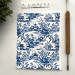 Puede incluir: Papel estampado en azul y blanco con un diseño repetido de pagodas, árboles y flores. El papel tiene un fondo blanco con detalles azules.