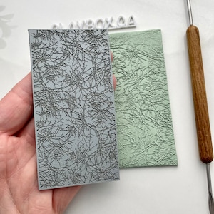 May include: Two gray textured polymer clay stamps with a branch pattern. The stamp on the left is a raised design and the stamp on the right is a recessed design.