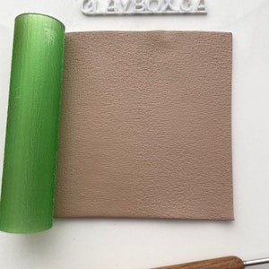 Peut inclure: Un rouleau vert texturé à côté d'un carré beige de matériau texturé. Le rouleau est cylindrique et translucide. Le matériau beige a une texture subtile et rugueuse. Le mot "CLAYBOX.CZ" est visible en lettres blanches.