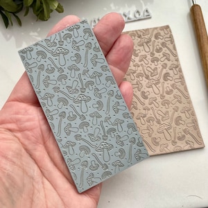 Op de afbeelding: Twee grijze en bruine rubberen stempels met een herhalend patroon van paddenstoelen. De stempels zijn ontworpen voor knutselen en het creëren van unieke ontwerpen.