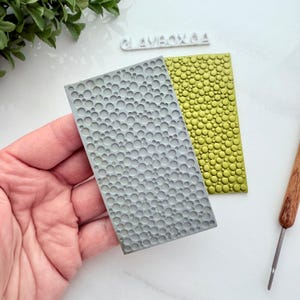 May include: Two silicone embossing mats with a raised bubble pattern. The mat on the left is gray and the mat on the right is green.