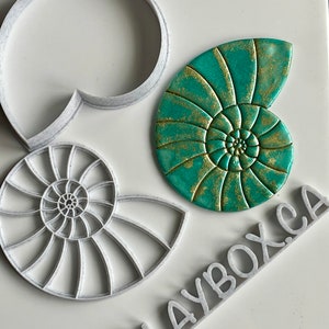 May include: A set of three white plastic moulds for making nautilus shell shapes. The moulds are shown with a green and gold nautilus shell made with the moulds. The moulds are labelled "CLAYBOX.CA".