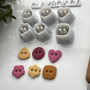 Peut inclure: Ensemble de 7 emporte-pièces en plastique blanc de différentes formes, notamment des cœurs, des fleurs et des boutons. Les emporte-pièces sont sur une surface blanche. CLAYBOX C4