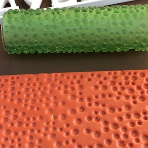May include: A green textured roller with a pattern of small circles. The roller is used to create a textured effect on surfaces.