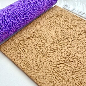 Peut inclure: Un rouleau à pâtisserie violet texturé est posé à côté d'une surface rectangulaire beige, présentant tous deux un motif texturé similaire. Les articles suggèrent un thème artisanal ou de pâtisserie, avec un design organique détaillé.