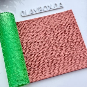 May include: A rolled-up, textured, bright green sheet next to a flat, textured, reddish-brown sheet. The word "CLAYBOX CA" is in white, raised letters in the background. The sheets have a repeating pattern.