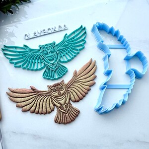 Könnte beinhalten: Drei eulenformige Bastelwerkzeuge. Eines ist ein türkisfarbener Kunststoffschneider, ein weiteres eine detaillierte gold-braune Eule und das dritte ein blauer Kunststoffschneider. Werkzeuge zum Basteln und Erstellen von Eulenmotiven.