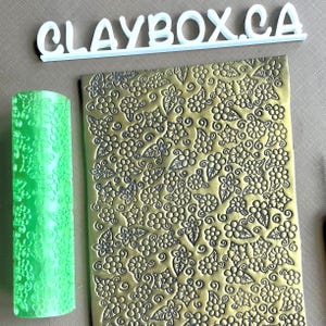 Puede incluir: Un rodillo verde con un patrón floral y una lámina de metal dorada con un patrón floral. La lámina de metal tiene el texto "CLAYBOX.CA" en ella.