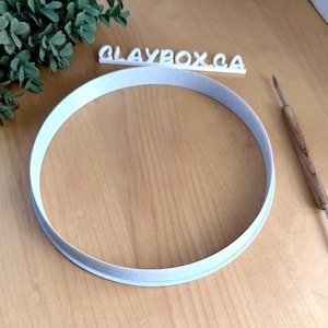 Può includere: Un tagliapasta rotondo in plastica bianca su una superficie di legno. Il tagliapasta ha un diametro di circa 15 cm.