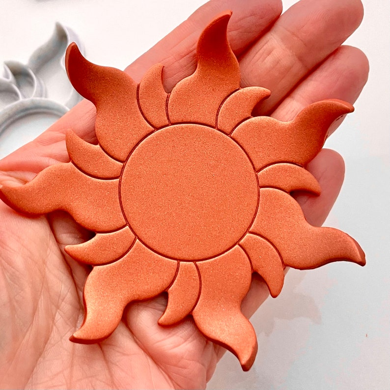 May include: A copper-colored sun with a raised, textured design. The sun has a circular center and 12 points radiating outward.
