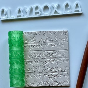 Peut inclure: Rouleau à pâtisserie vert avec un motif de feuilles, utilisé pour créer un motif en relief sur une pièce d'argile. L'argile présente un motif de feuilles similaire, montrant l'effet du rouleau à pâtisserie.