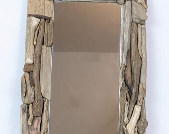 Peut inclure: Un miroir rectangulaire avec un cadre composé de divers morceaux de bois flotté. Les morceaux de bois flotté sont dans des tons de brun, beige et gris, créant une esthétique naturelle et rustique. La surface réfléchissante du miroir est de couleur brun clair.