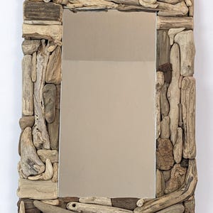 Könnte beinhalten: Rechteckiger Spiegel mit einem Rahmen aus Treibholzstücken in verschiedenen Größen und Formen in Beige-, Braun- und Grautönen. Die reflektierende Oberfläche des Spiegels hat einen hellen, neutralen Farbton.