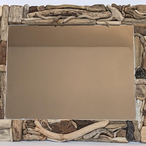 Può includere: Specchio rettangolare con cornice realizzata con vari pezzi di legno trasportato dall'acqua. La cornice è composta da pezzi di legno marrone chiaro e scuro, creando un'estetica naturale e rustica. La superficie dello specchio riflette una parete dai toni neutri.